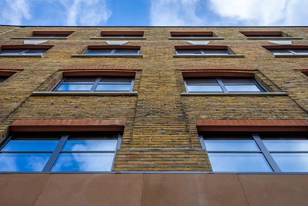 The refurbished Drury Works building in London. The photo is taken from the ground looking upwards and shows the handmade yellow brick slip cladding used as part of the external renovations.